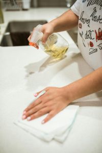 A woman cleaning a kitchen counter with a spray bottle and cloth indoors, depicting household chores.