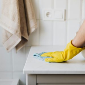 Close-up of a person wearing yellow gloves wiping a bathroom counter with a cloth.